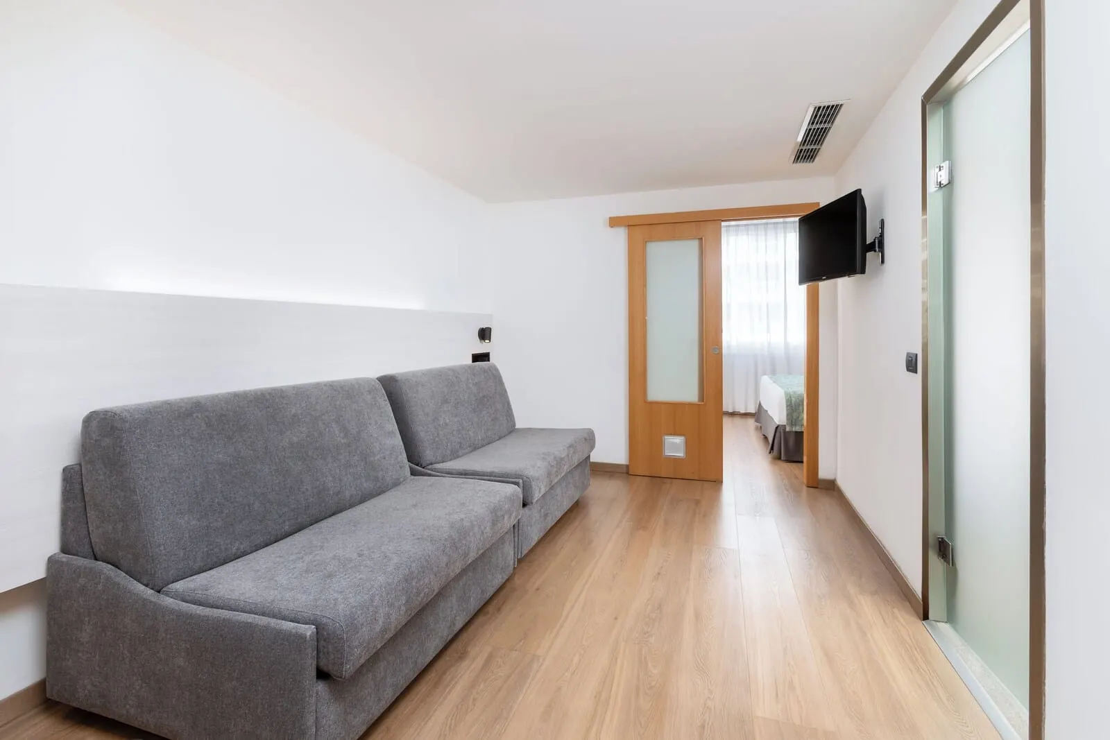 Alexandre Troya: A modern room with a grey sofa, wooden flooring, a TV mounted on the wall