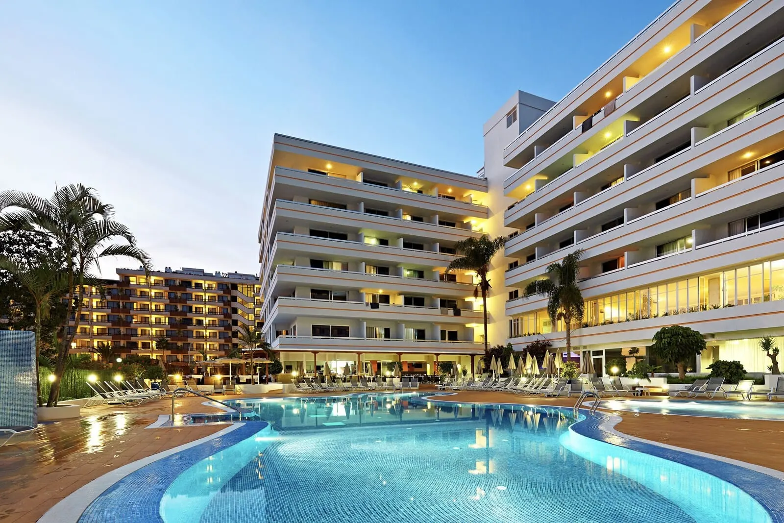 Coral Suites & Spa: A hotel with a swimming pool, multiple balconies, and a well-lit facade