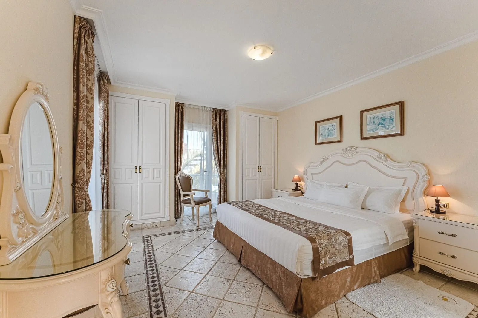 Flamingo Suites Boutique Hotel: A bedroom with a large bed, a glass-topped dresser, a chair, and a window with curtains
