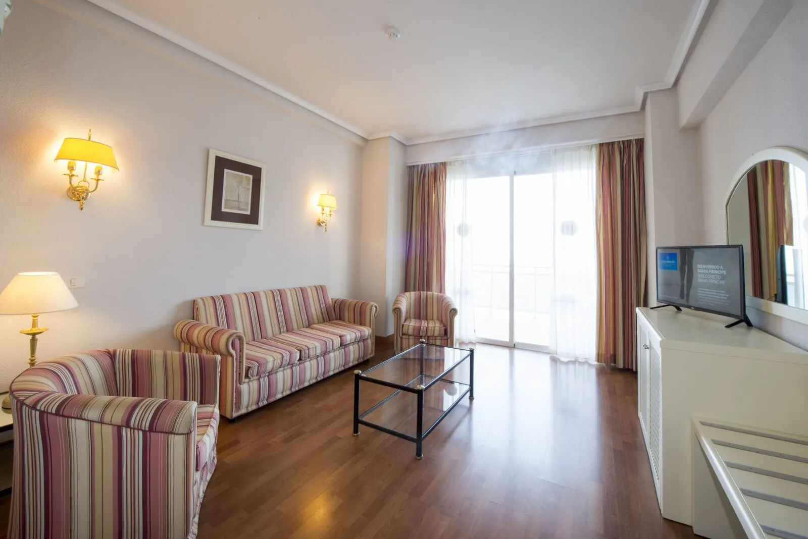 Bahia Principe Explore San Felipe: A living room with striped sofas, a glass coffee table, a TV, and a radiator