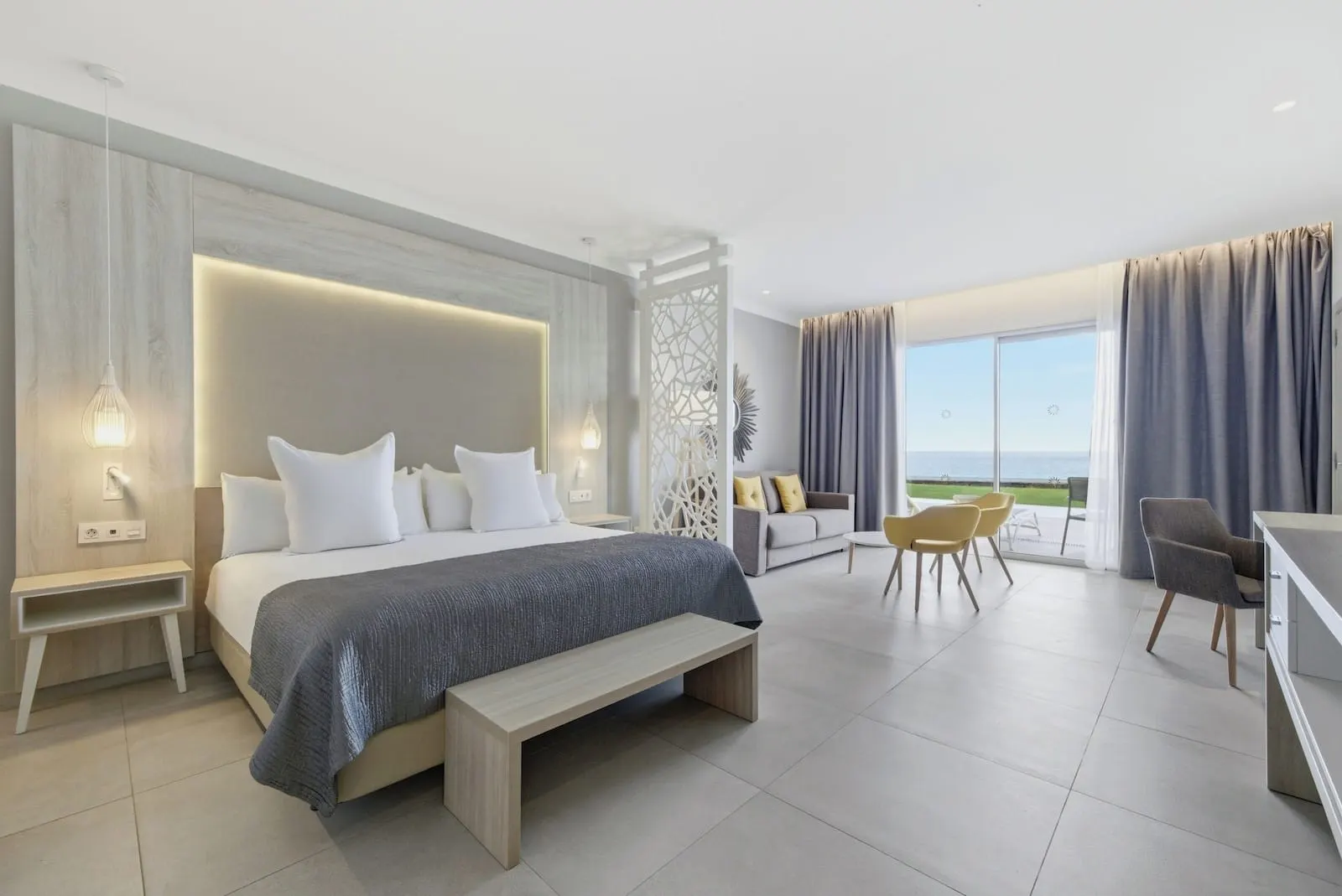 Bahia Principe Explore Fantasia: A modern bedroom with a large bed, bedside tables, a bench, a sofa