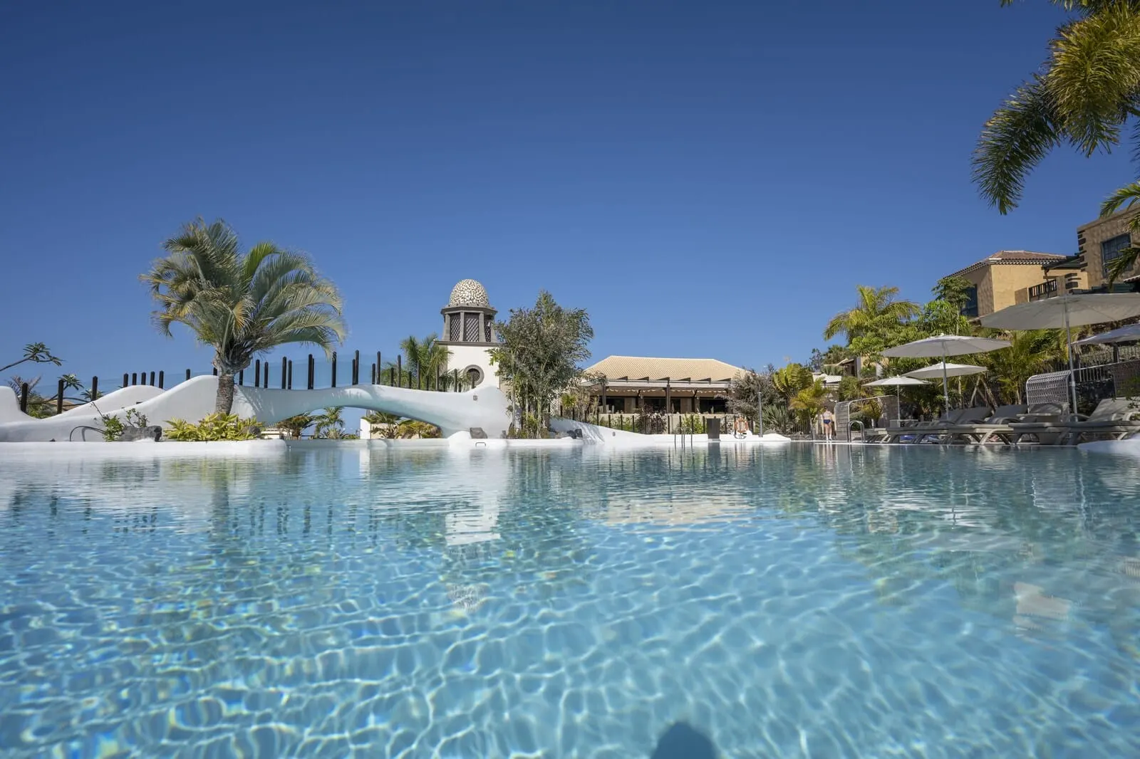 Hotel Suite Villa María: A clear pool with lounge chairs and umbrellas, palm trees
