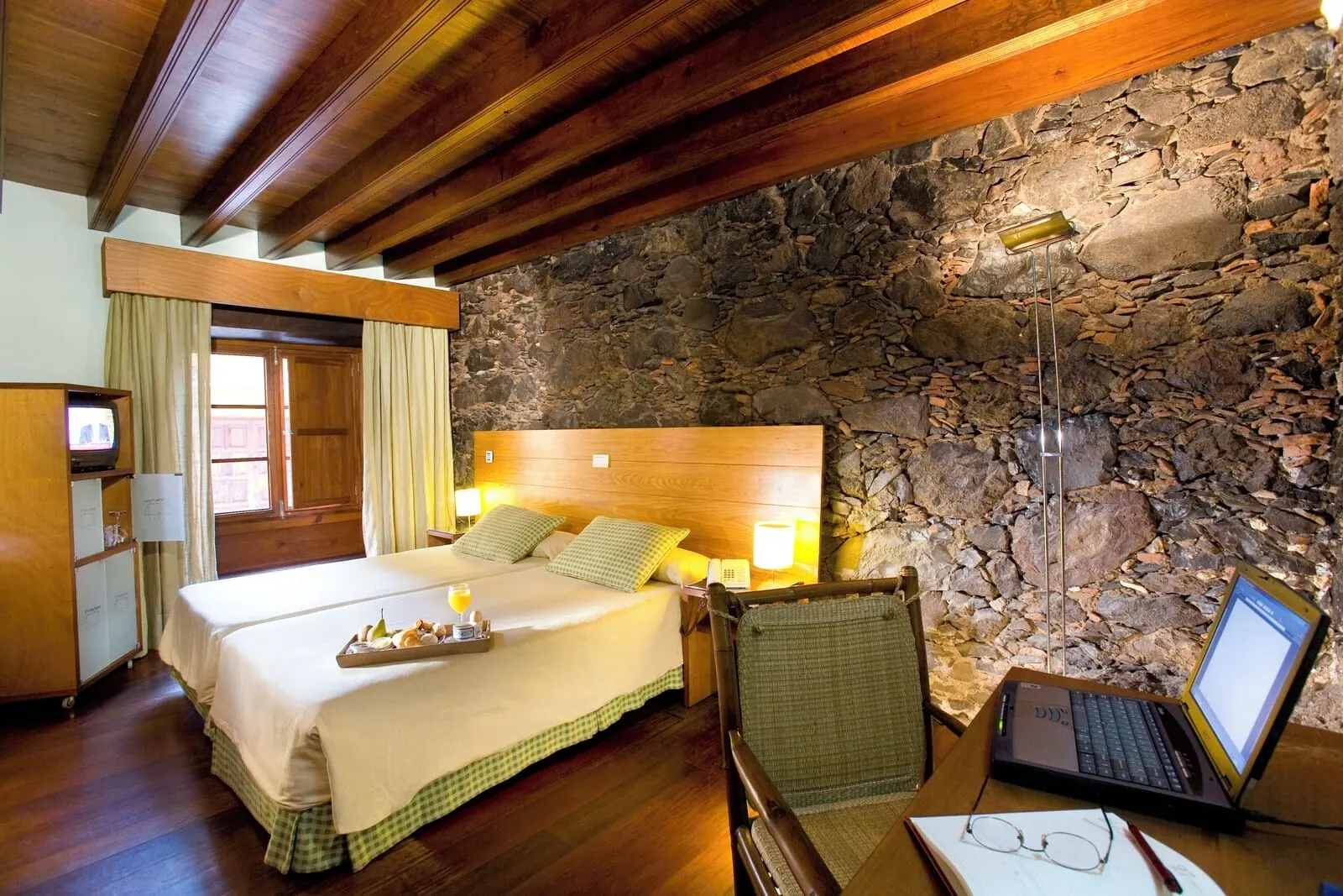 Hotel La Quinta Roja: A hotel room with a stone wall, wooden ceiling beams, a bed with a tray of fruit