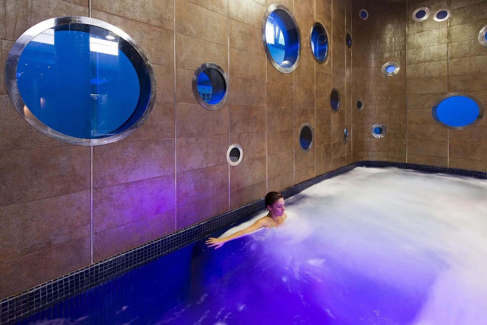 Marylanza Suites & Spa: A person in a large indoor pool with multiple circular windows on the walls