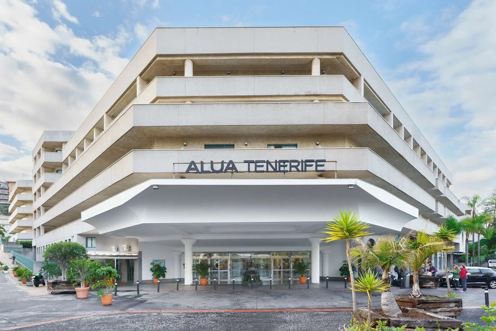 Alua Tenerife: A multi-story hotel with balconies, a central entrance, and potted plants