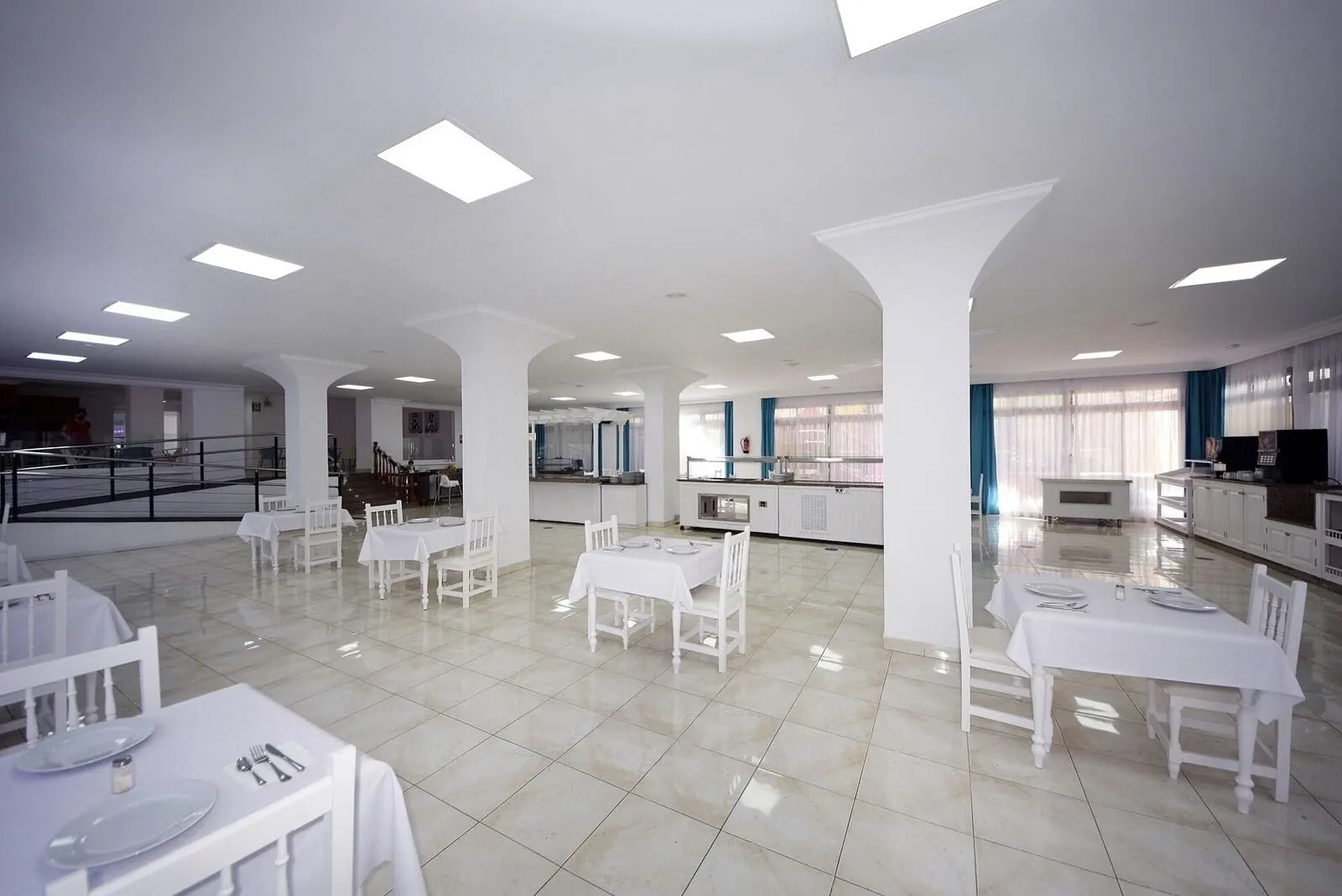 Skyview Hotel by LIVVO: A spacious dining area with white tables and chairs, a kitchen area with a counter