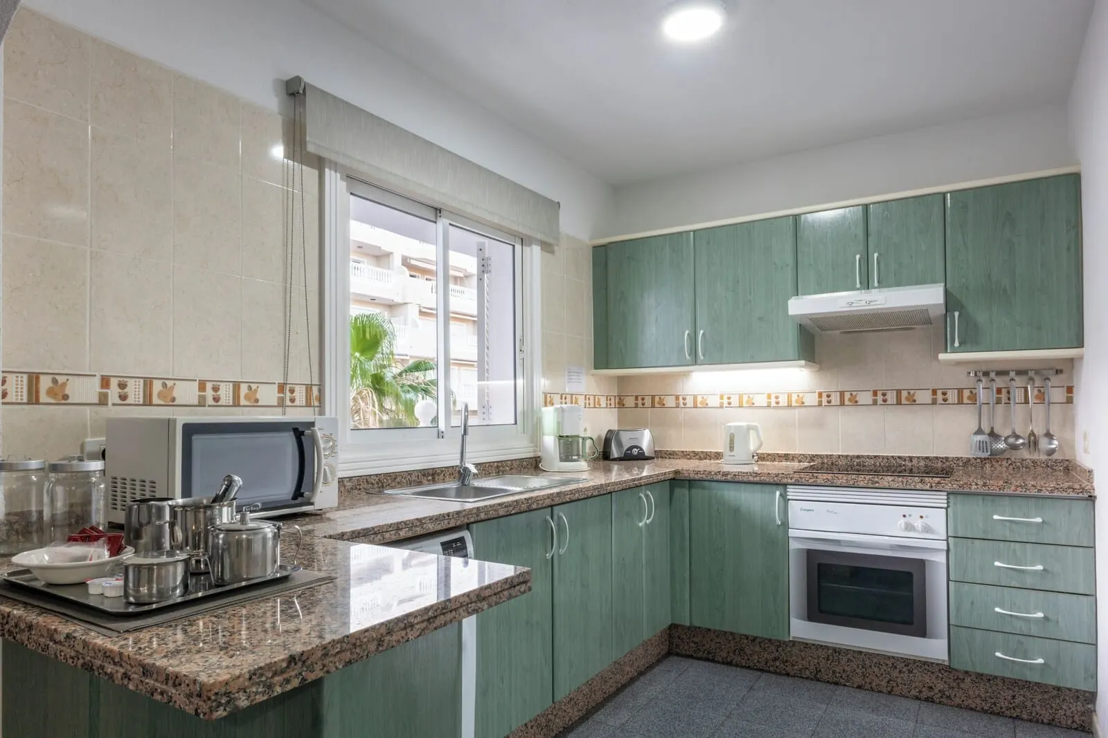 Ona El Marqués: A kitchen with green cabinets, a microwave, a toaster, and a stove