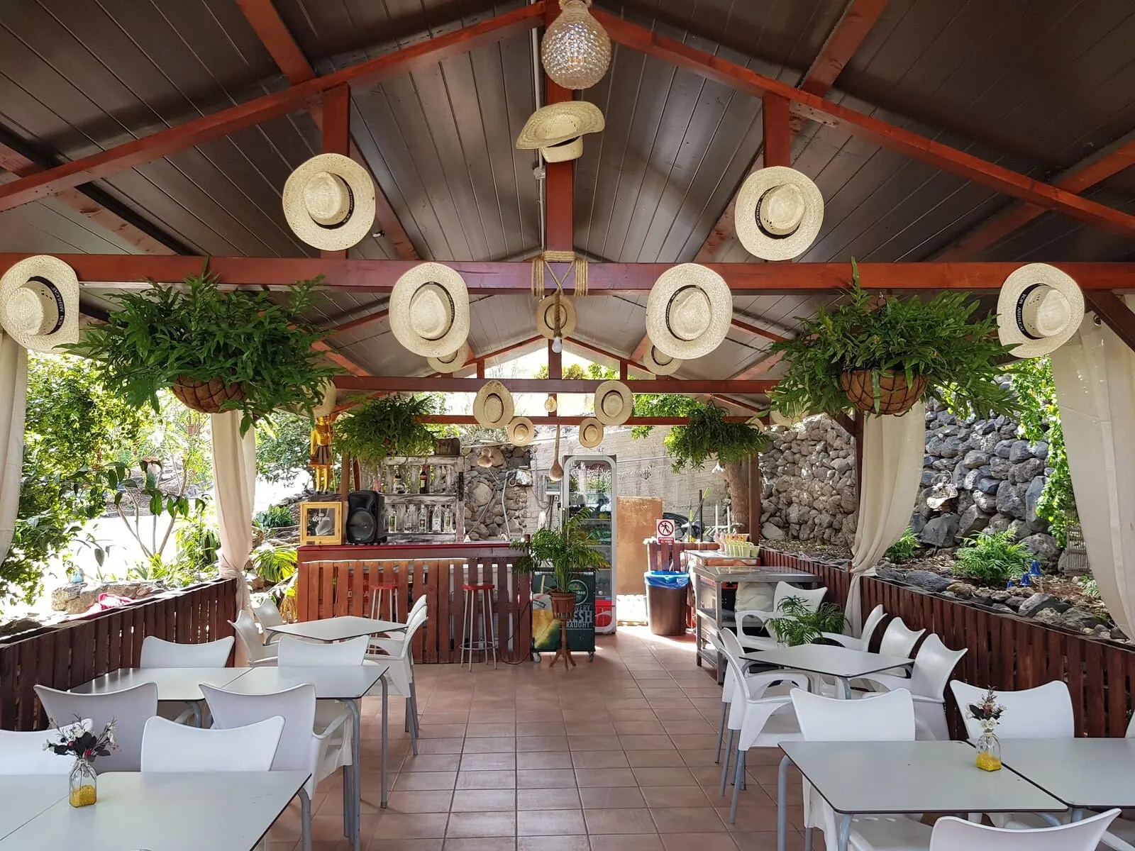 Hotel Rural La Raya 1866: An outdoor restaurant with white tables and chairs, a bar area, and hanging hats