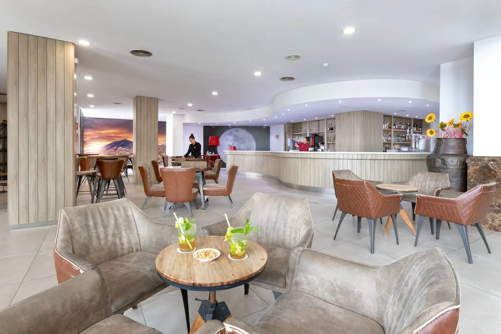 Alexandre Gala: A modern hotel lobby with seating areas, a bar, and a large mural of a sunset