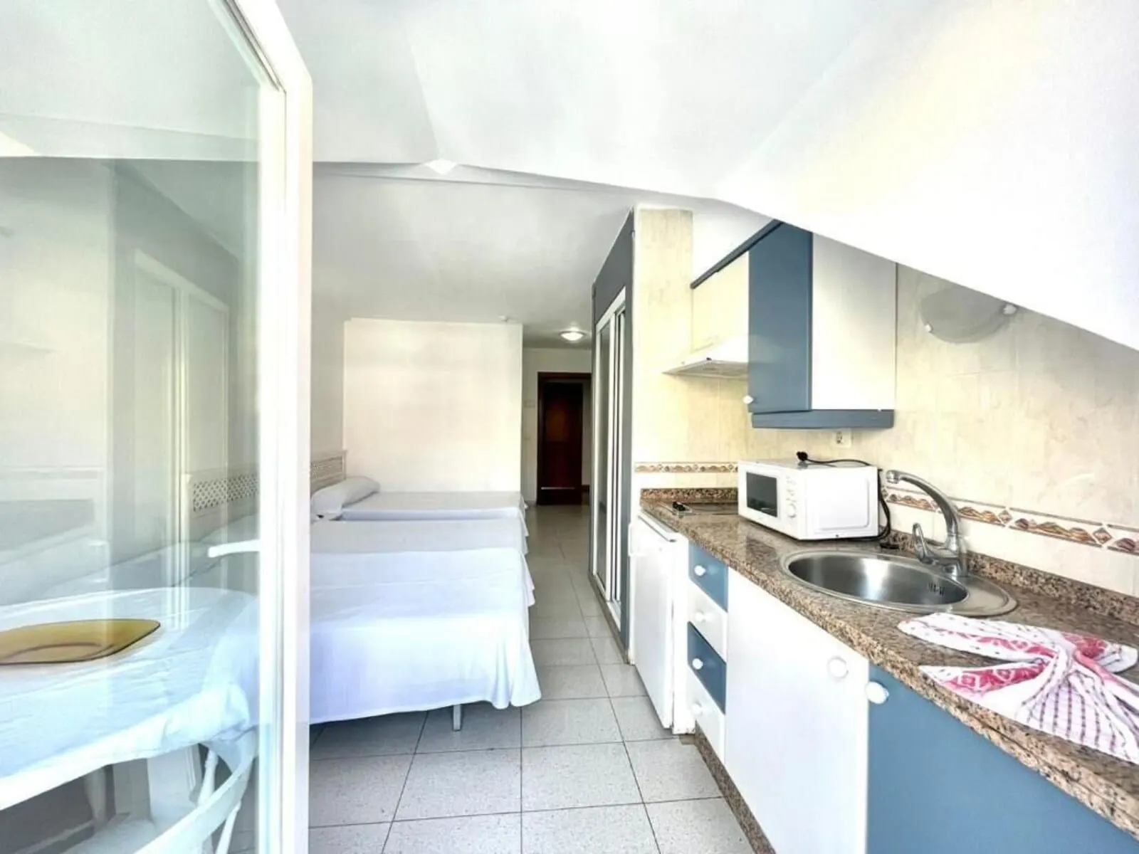 Apartamentos Pez Azul: A compact hotel room with a kitchenette, a bed, and a glass door leading to a balcony