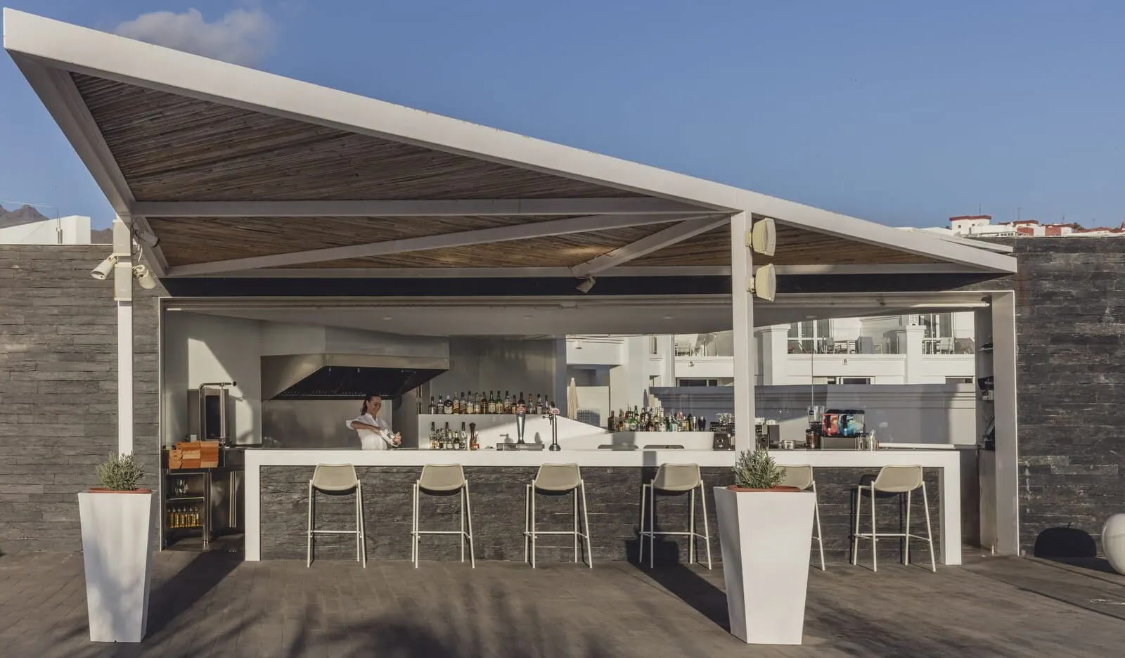 Flamingo Beach Mate: An outdoor bar area with a chef preparing drinks, a bar counter, and several stools