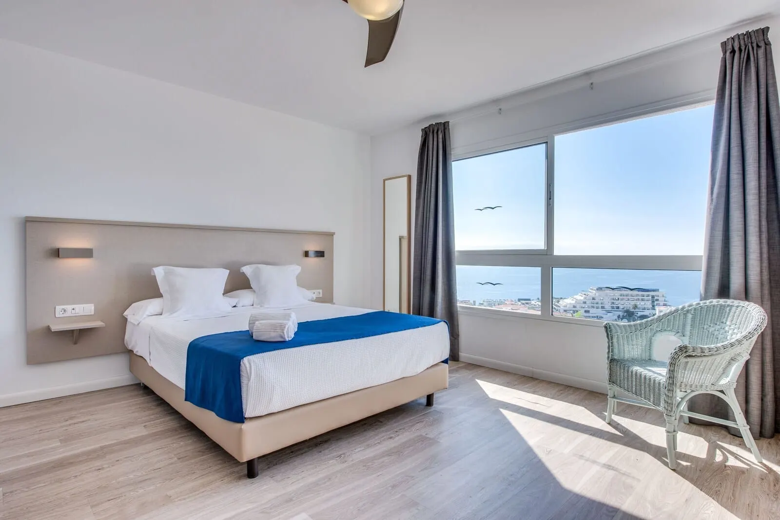 Vigilia Park: A modern hotel room with a large bed, a view of the sea, and a wicker chair