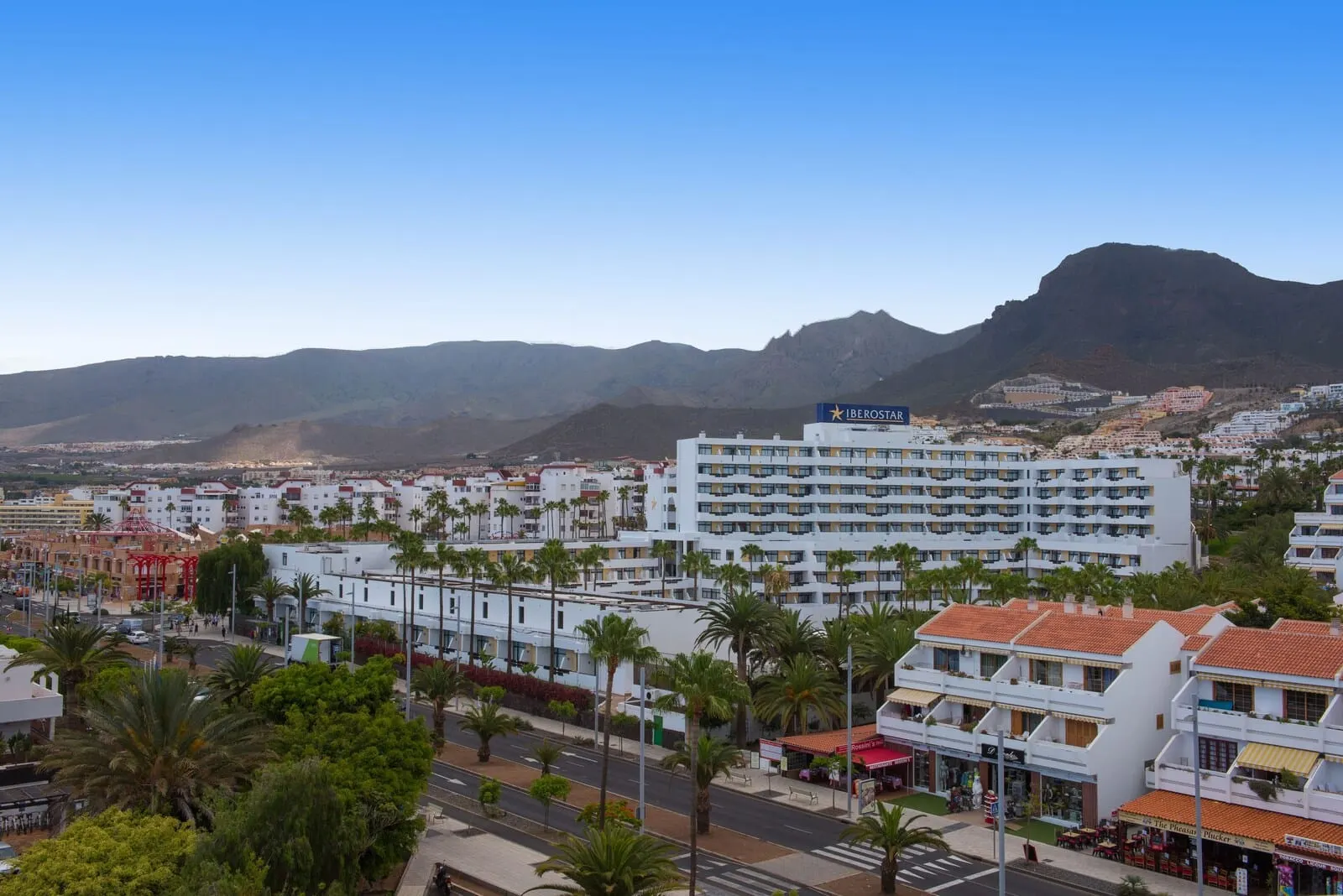 Iberostar Waves Bouganville Playa: A coastal hotel with multiple floors, balconies, and a view of the sea and mountains
