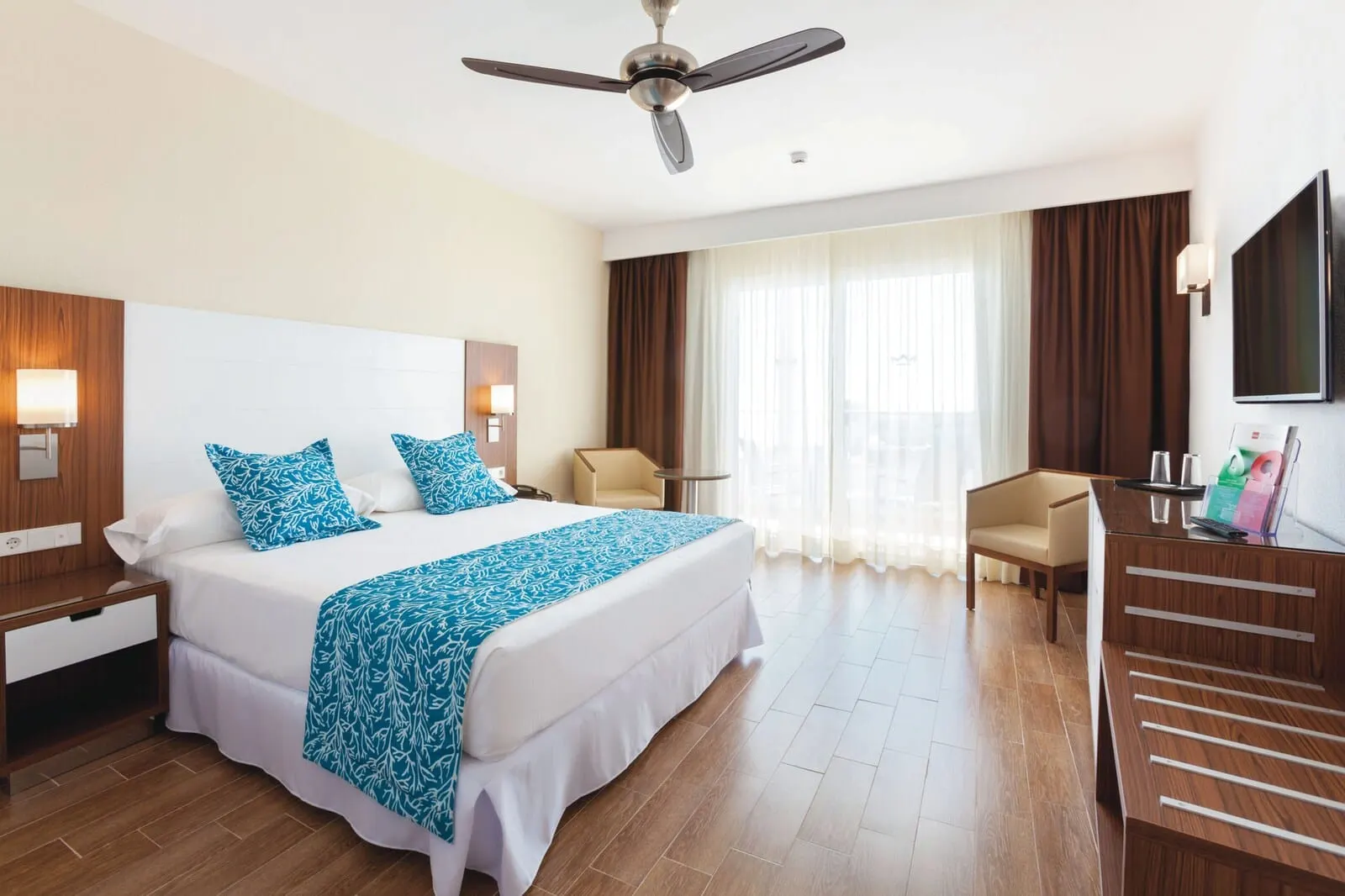 Hotel Riu Arecas: A hotel room with a large bed, a desk, a chair, a ceiling fan, and a TV