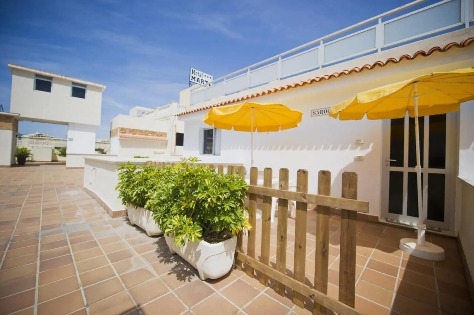 Hotel Marte: A hotel exterior with a tiled patio, yellow umbrellas, and potted plants