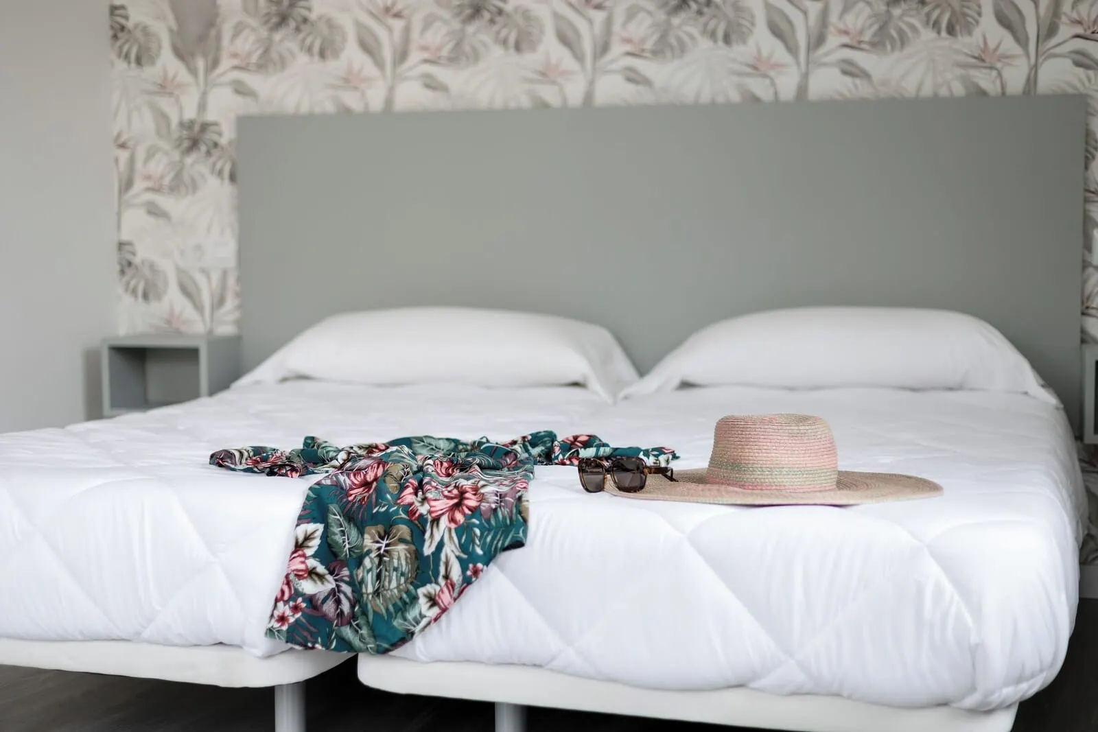 Hotel Boutique HC Maga: A neatly made bed with a floral-patterned blanket and a straw hat on it