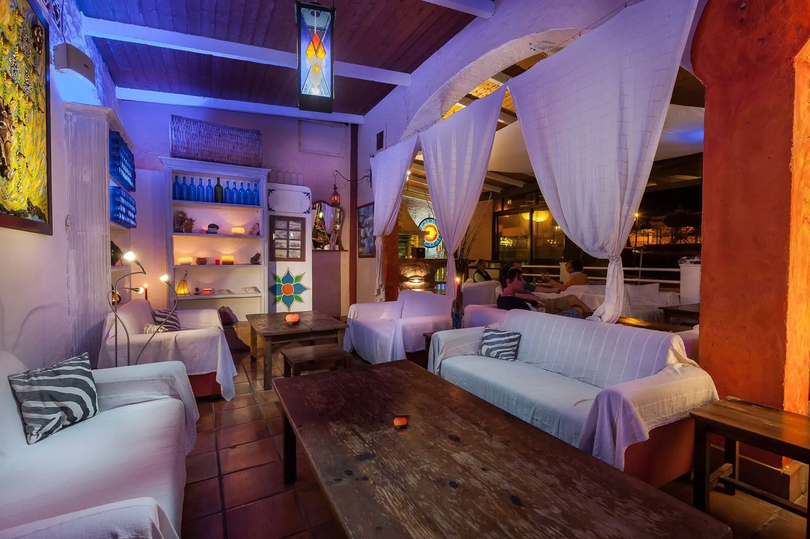 Rok Plaza: A cozy, dimly lit room with a wooden table, two white sofas, and a bookshelf
