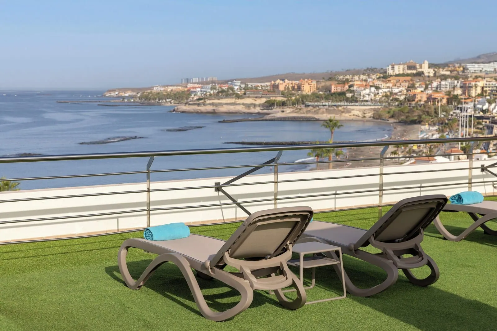 AluaSoul Costa Adeje: A balcony with two lounge chairs and a railing overlooking a beach and cityscape