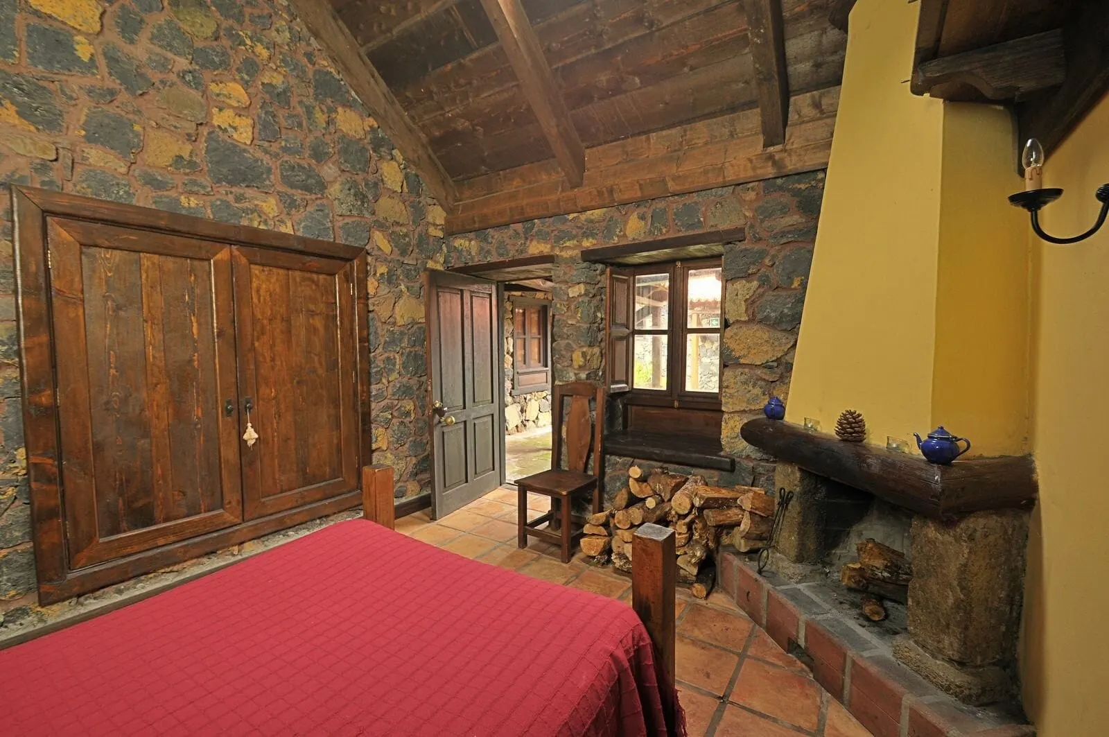 Hotel Rural Caserío Los Partidos: A rustic room with a wooden bed, stone walls, a fireplace, and a wooden ceiling