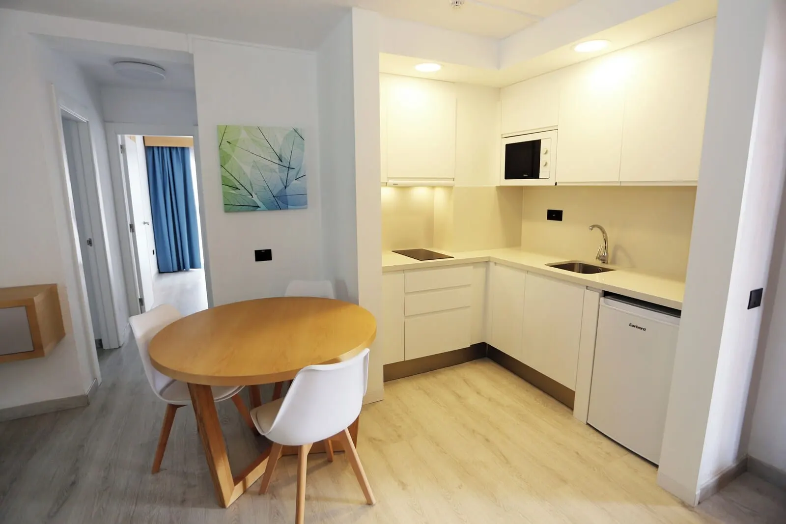 Hotel Andorra: A modern kitchen with white cabinets, a wooden dining table, and a built-in microwave