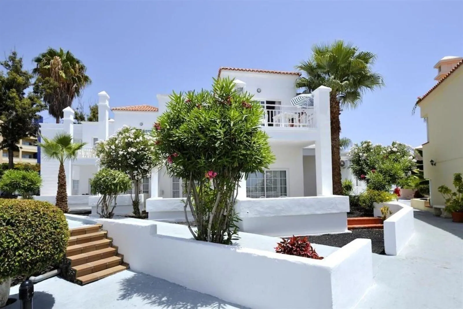 BLUESEA Bahía Fañabé Villas: A white building with a balcony, surrounded by greenery and palm trees