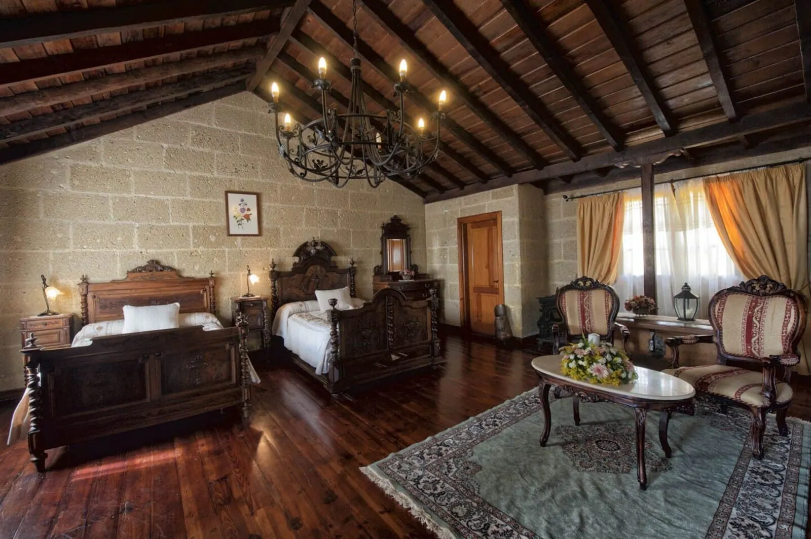 Hotel Rural Senderos de Abona: A traditional room with a wooden bed, a chandelier, and a stone wall