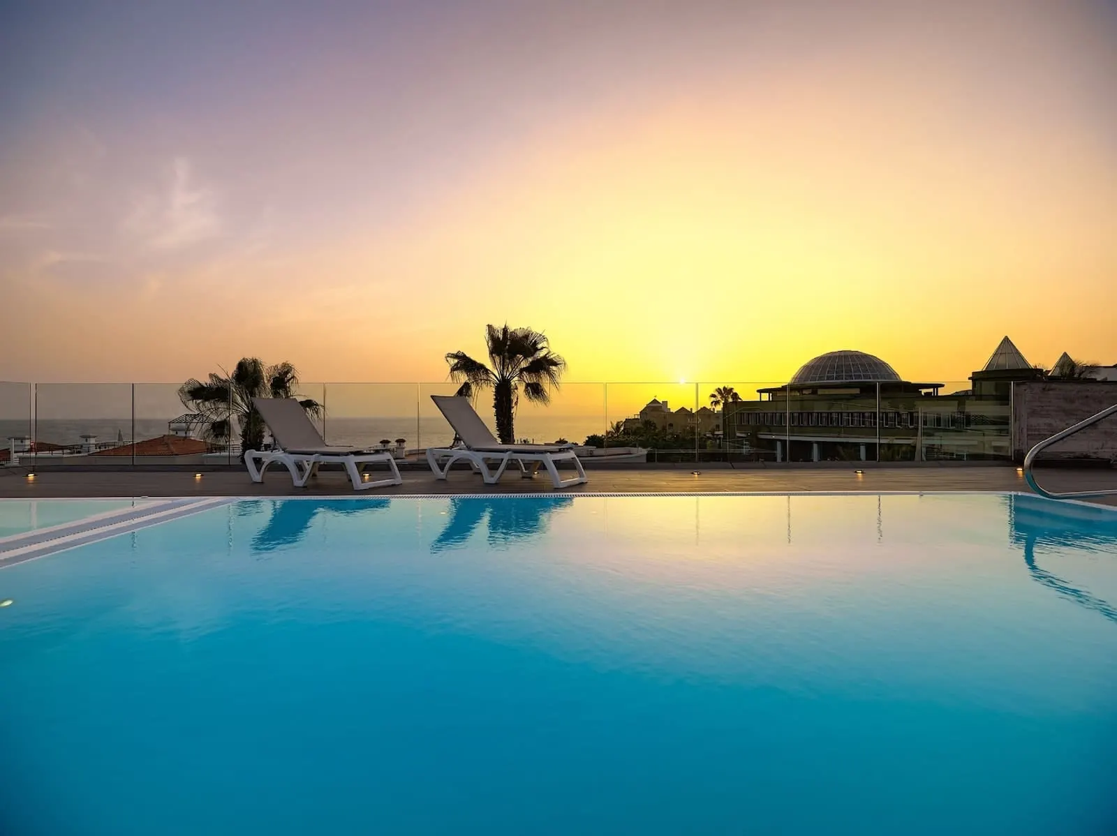 Hotel Colón Guanahaní: A pool with lounge chairs, palm trees, and a sunset view