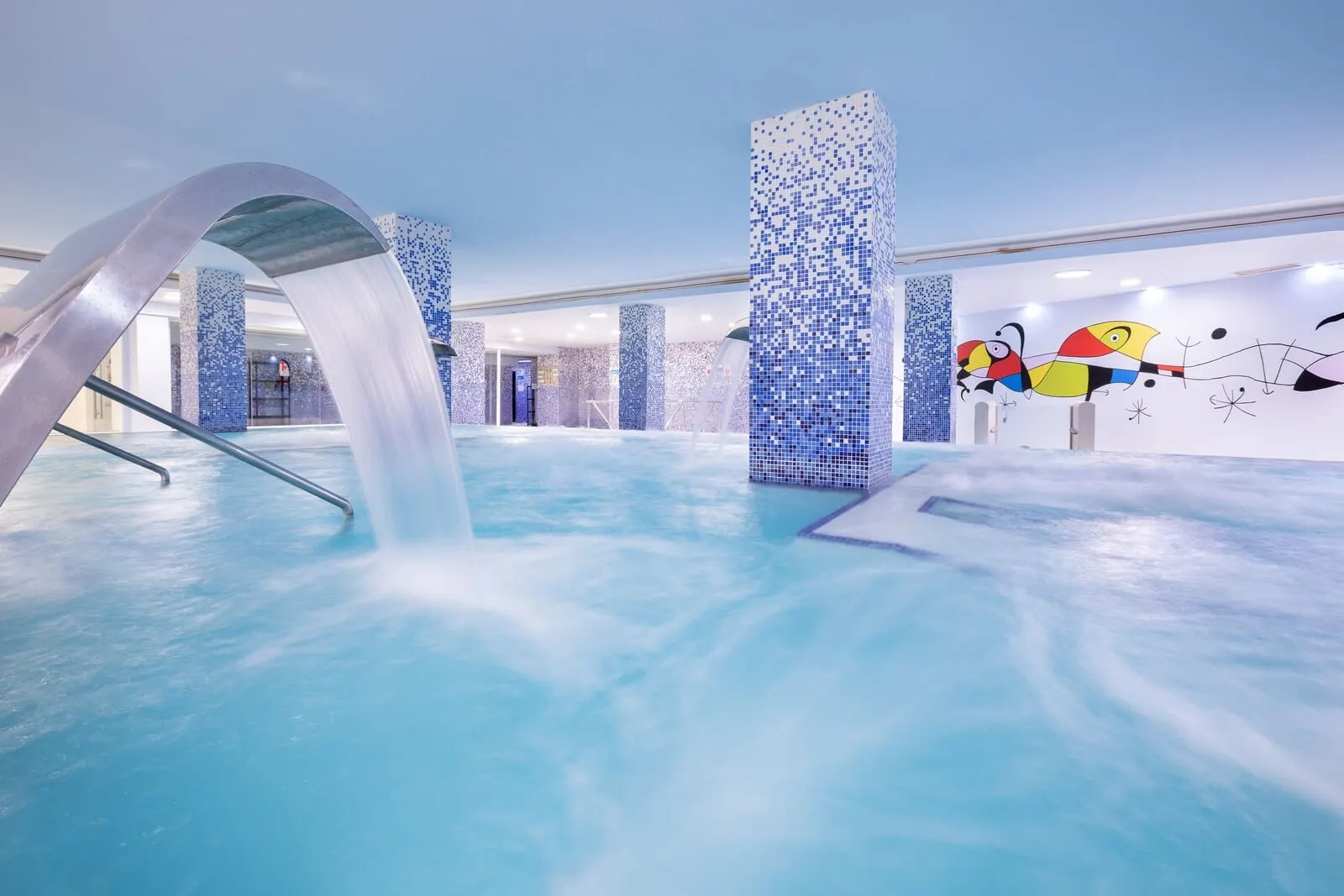 Alexandre Gala: An indoor swimming pool with a water feature, tiled walls, and abstract wall art