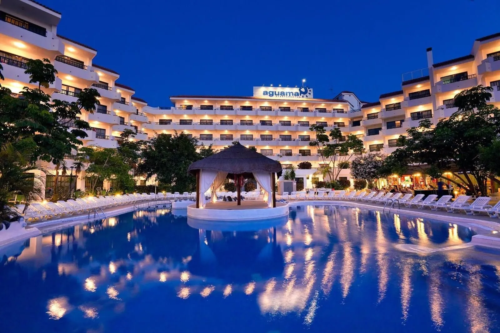 Apartamentos Aguamar: A hotel with a large pool, multiple balconies, and a well-lit facade