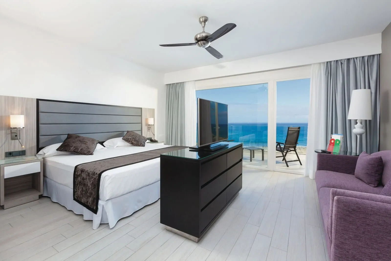 Hotel Riu Palace Tenerife: A modern hotel room with a bed, a desk, a chair, and a view of the ocean