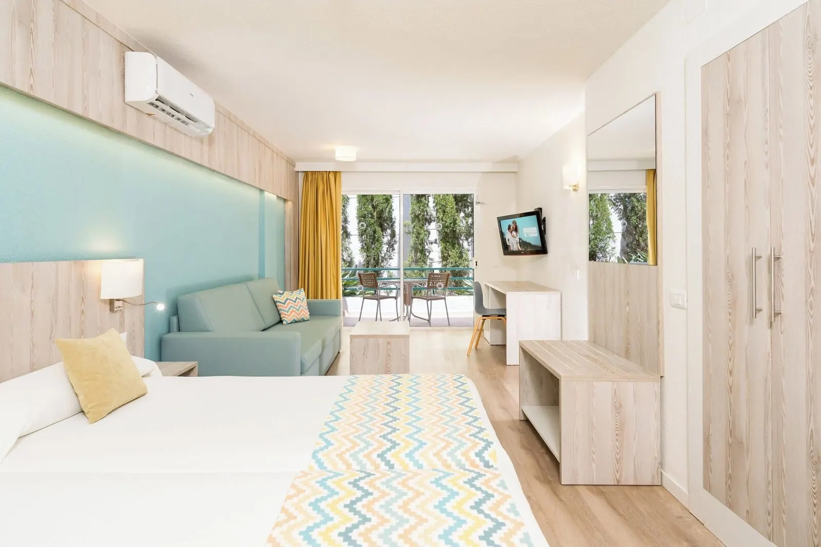 HOVIMA Panorama: A modern hotel room with a bed, a sofa, a desk, and a balcony with a view of trees