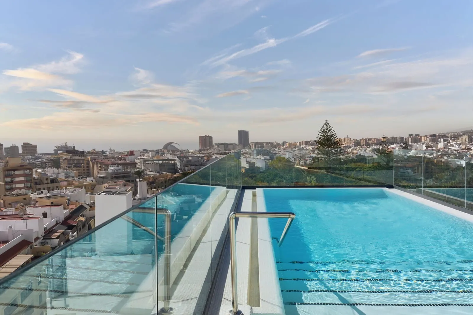 Barceló Santa Cruz Contemporáneo: A rooftop infinity pool with a city view, glass railings, and a clear sky