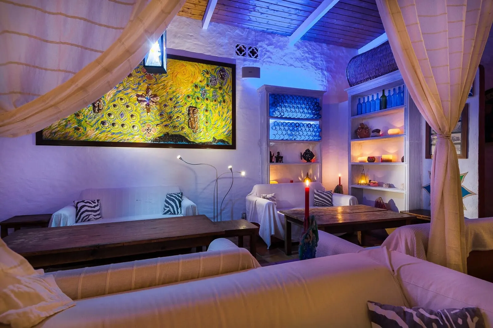 Rok Plaza: A cozy room with a large painting, a shelf with bottles, and a candle on a table