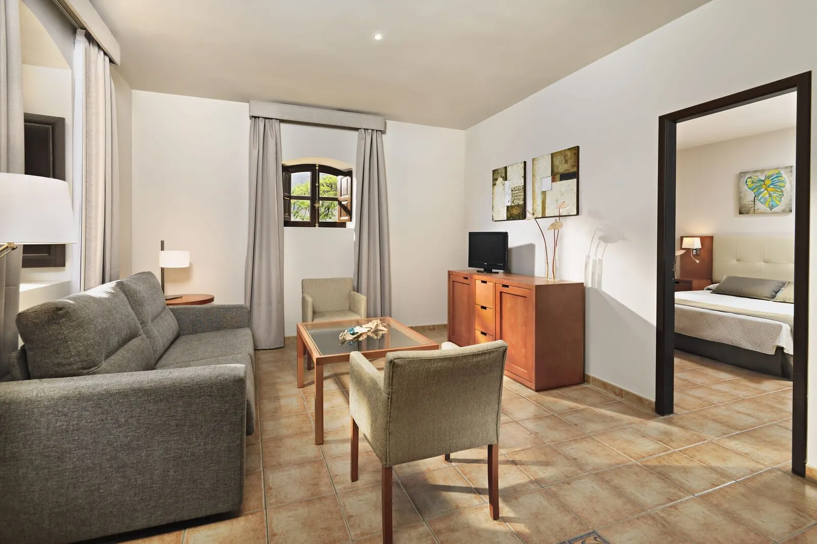 Hotel Rural Finca Salamanca: A modern hotel room with a sofa, armchair, and a small table. There is a TV, a cabinet