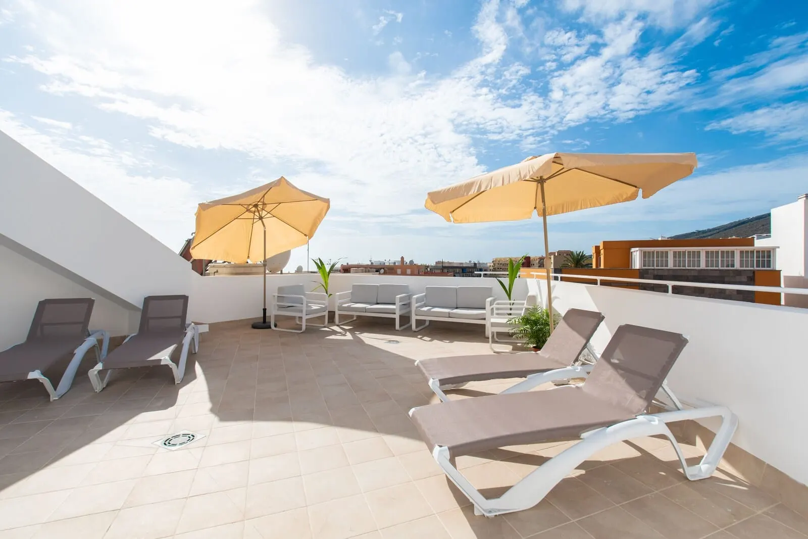 Suncanarias Hotel Adeje Plaza: A rooftop terrace with sun loungers and umbrellas, a small table, and potted plants