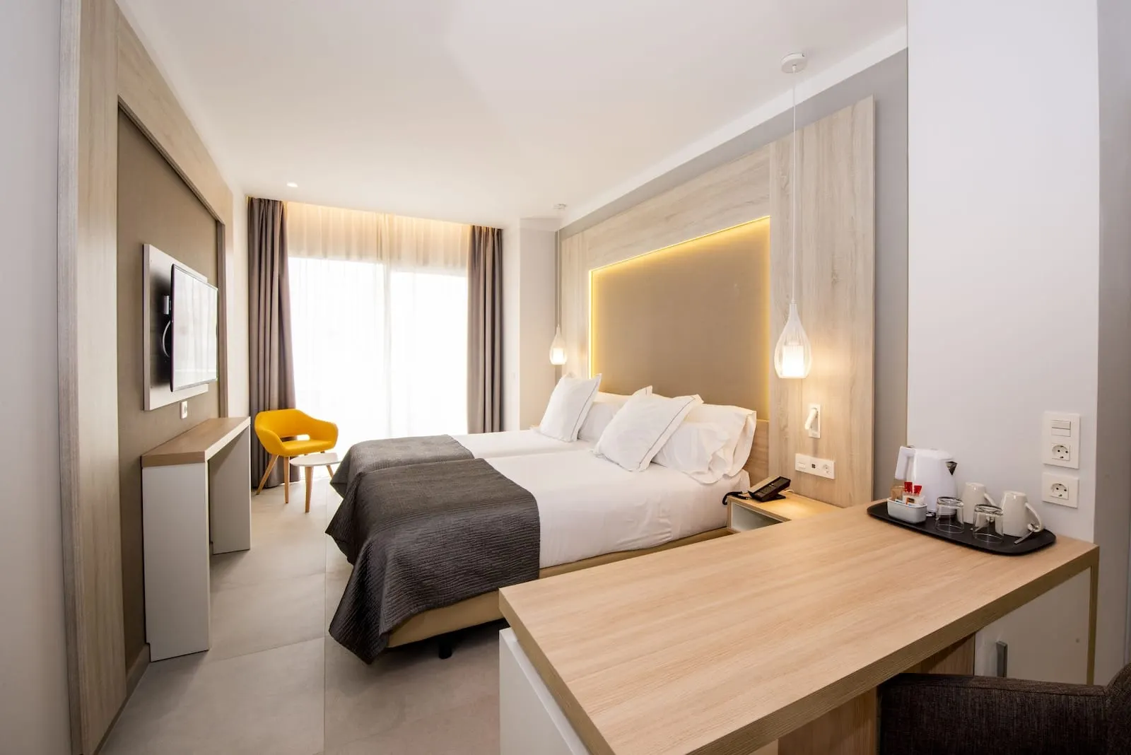 Bahia Principe Explore Fantasia: A hotel room with a bed, bedside table, desk, chair, and a TV on the wall