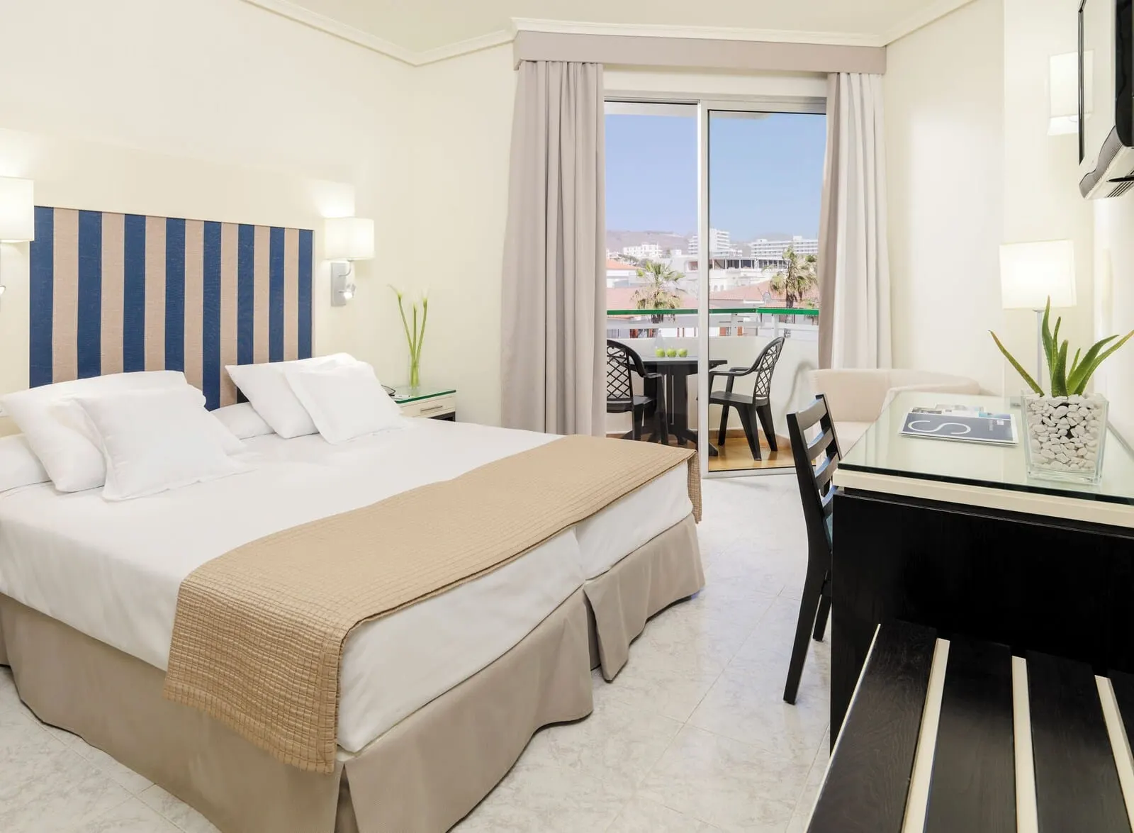 H10 Las Palmeras: A hotel room with a bed, a desk, and a balcony with a view of buildings