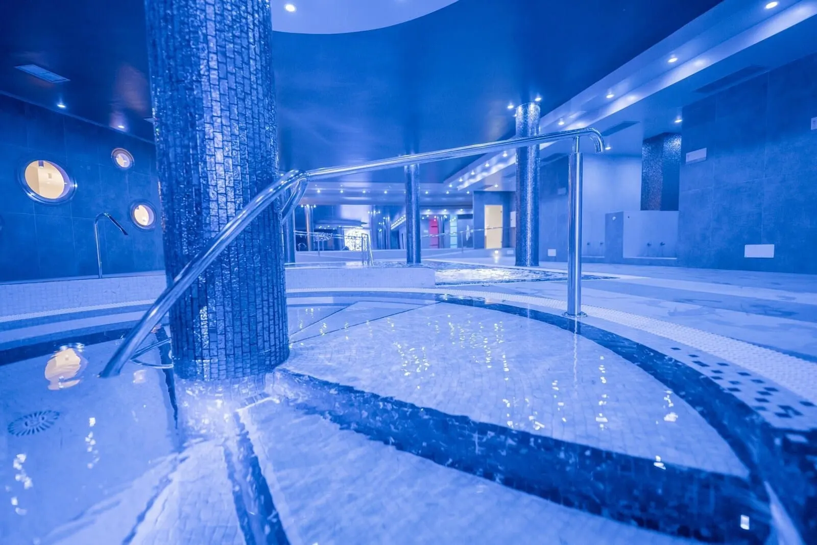 Atlantic Mirage Suites & Spa: A modern indoor pool area with a tiled floor, a central column, and a metal handrail