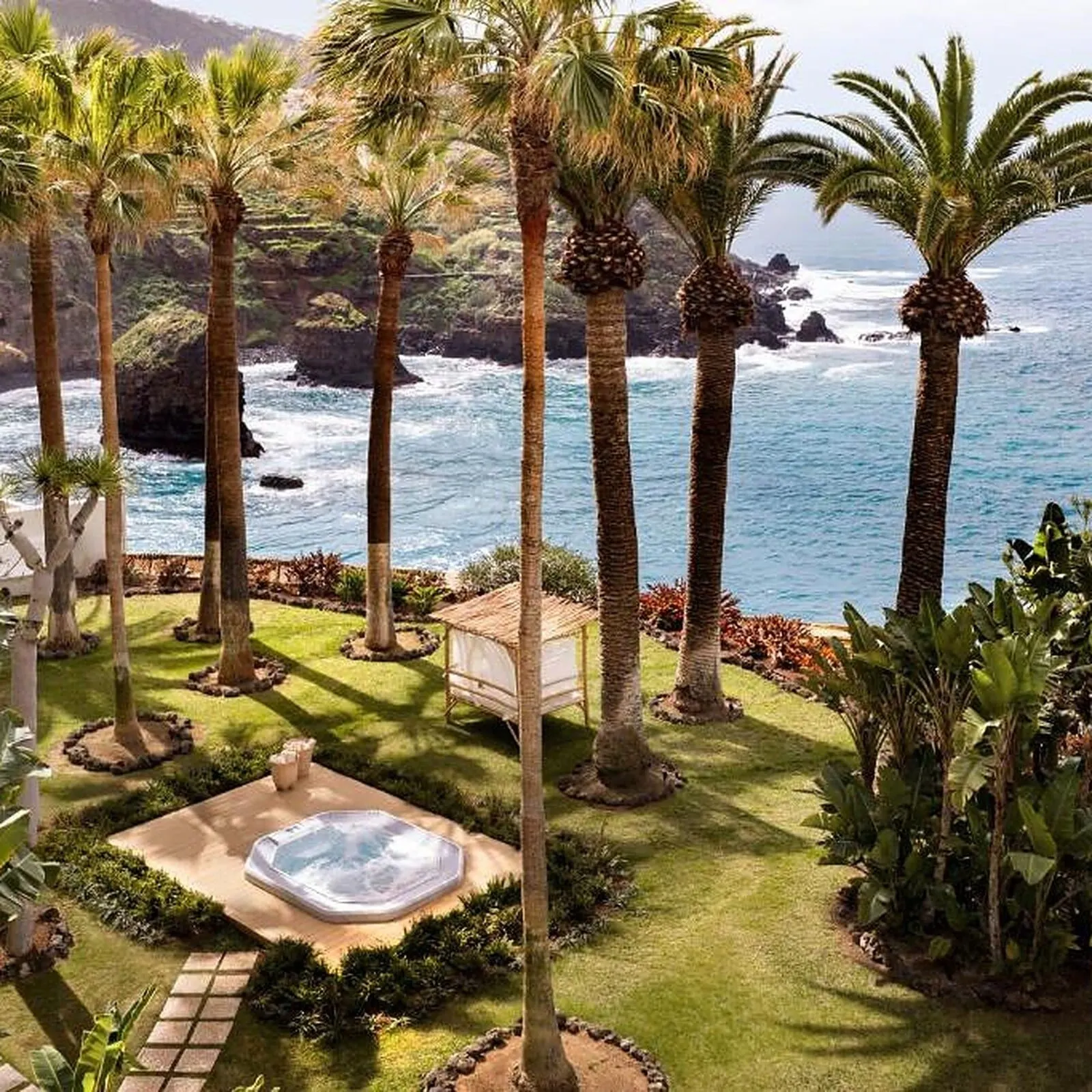 Precise Resort Tenerife: A landscaped garden with palm trees, a hot tub, and a view of the ocean