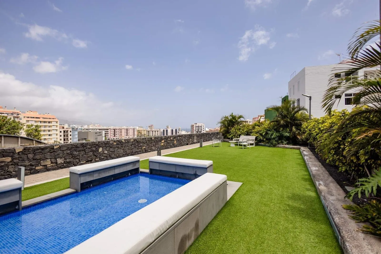 Hotel Escuela Santa Cruz: A rooftop pool with a stone wall, green lawn, and a view of the cityscape