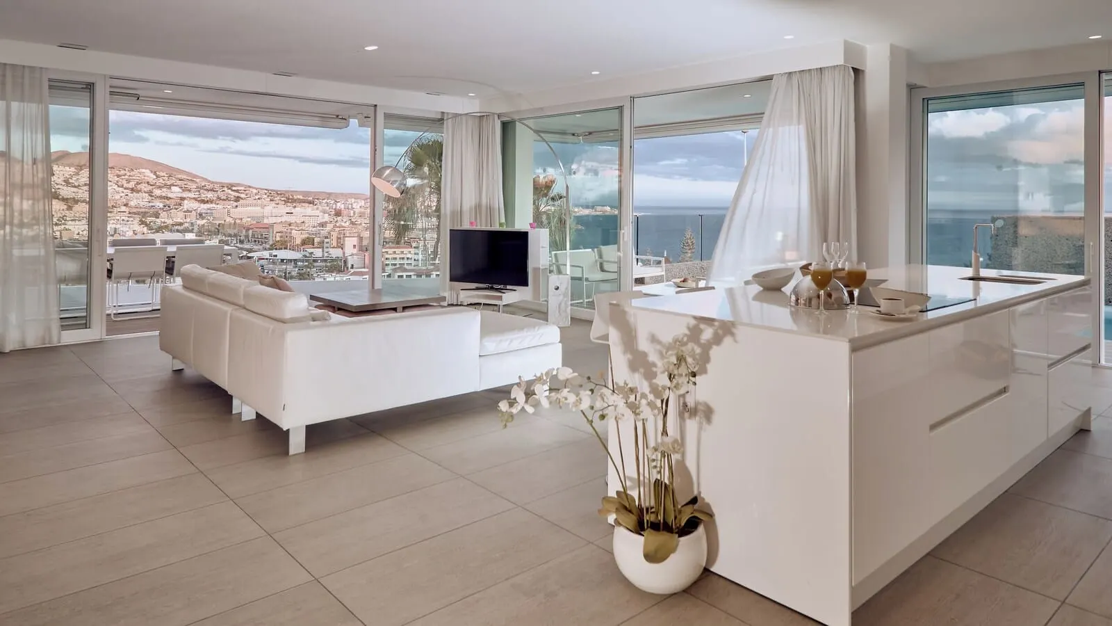 Domes Baobab Suites: A modern living room with a sofa, TV, and dining area with a view of the city and sea