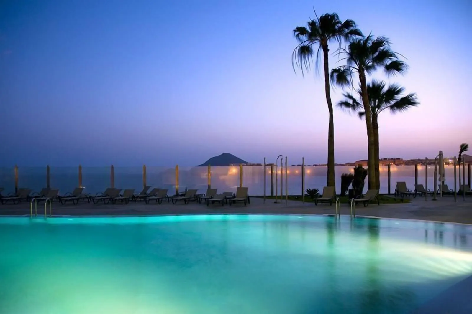 KN Hotel Arenas del Mar: A poolside view with lounge chairs and palm trees at dusk