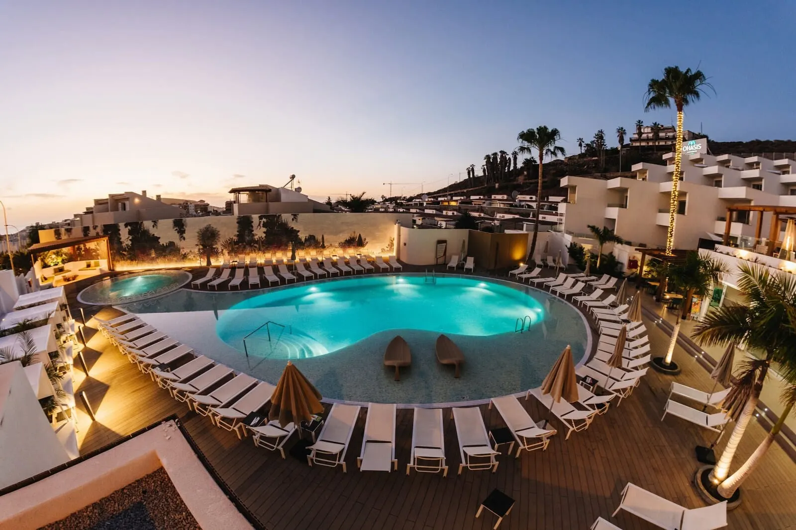 Ohasis Boutique Suites: A pool area with lounge chairs and umbrellas, surrounded by buildings and palm trees