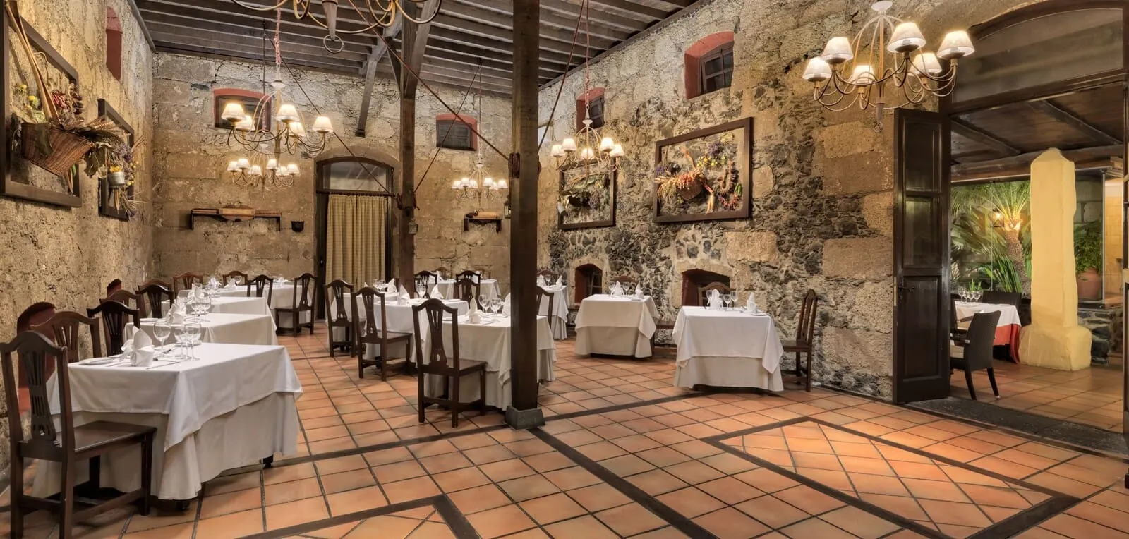 Hotel Rural Finca Salamanca: A restaurant with multiple tables and chairs, stone walls, and hanging chandeliers
