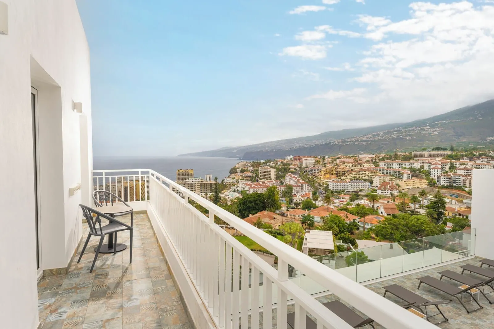 TUI BLUE Atlantic Hills: A balcony with a view of a coastal town, a table with chairs, and a glass railing