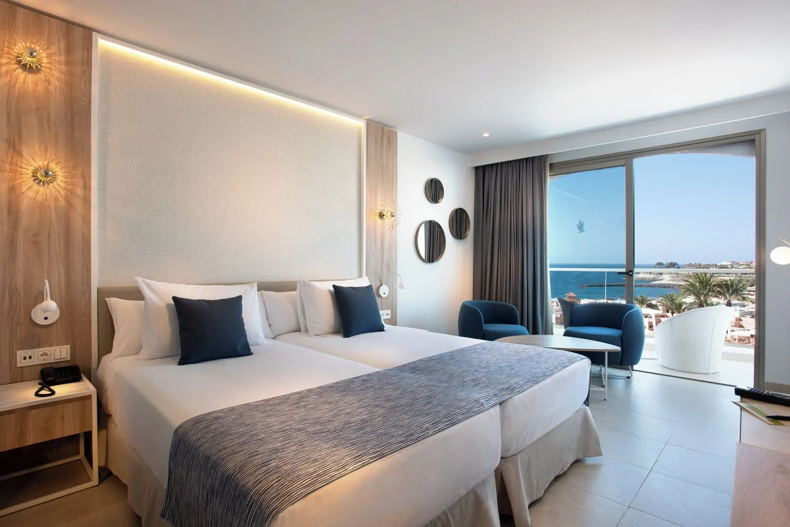 Guayarmina Princess: A modern hotel room with a large bed, a desk, a chair, and a view of the sea