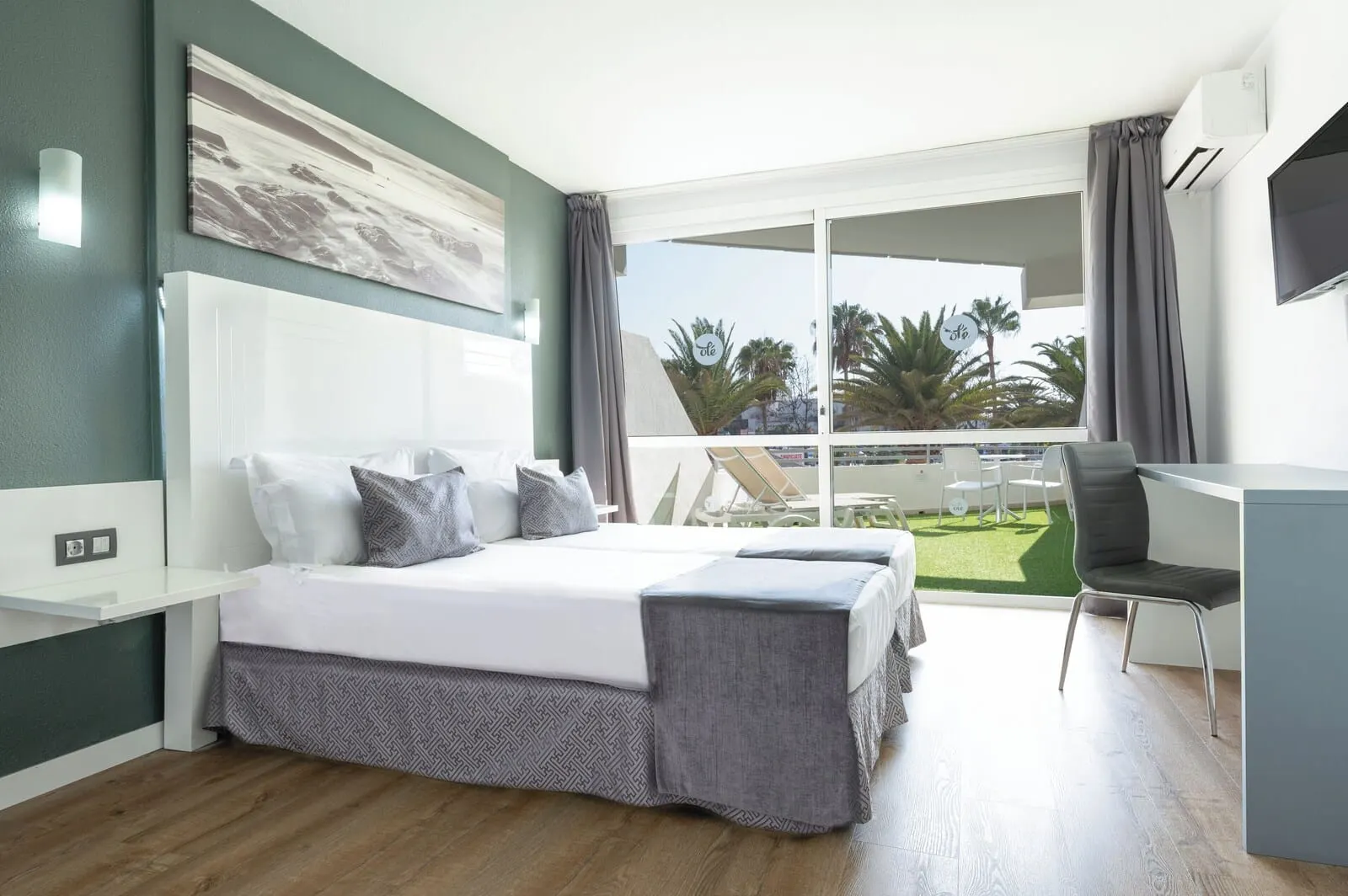 Olé Tropical Tenerife: A modern hotel room with a large bed, a desk, and a balcony with a view of palm trees