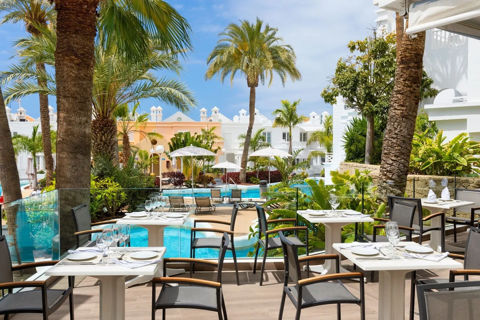 Lagos de Fañabé Beach Resort: An outdoor dining area with tables and chairs, a pool, and palm trees