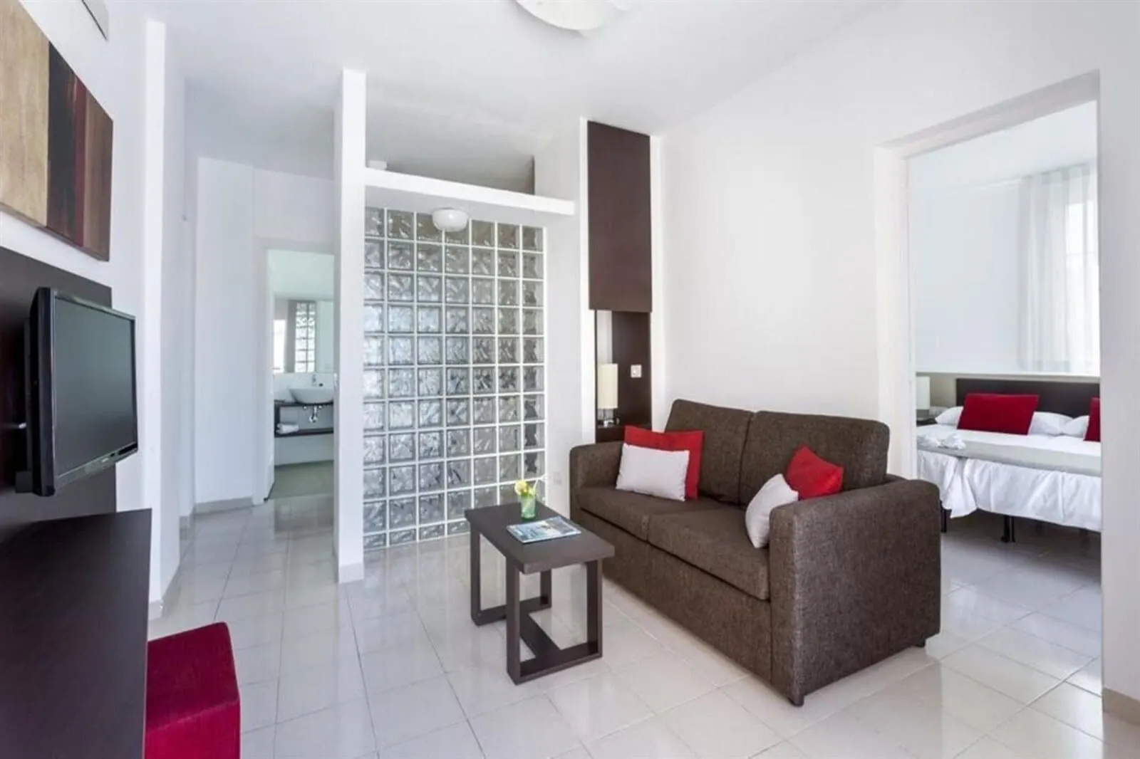 BLUESEA Bahía Fañabé Villas: A modern hotel room with a sofa, a coffee table, a TV, and a large window