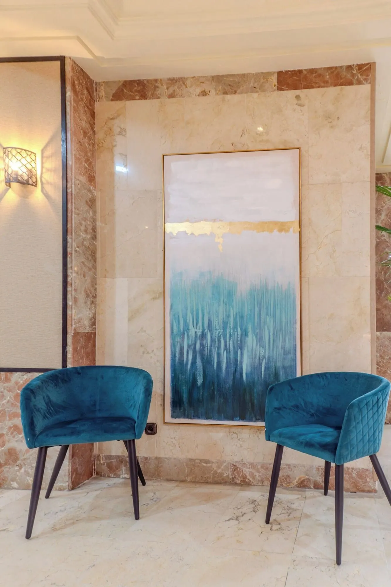 Hotel Aeropuerto Sur: A room with two teal velvet chairs, a marble wall, and a large abstract painting